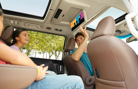 Man in front seat of vehicle opening rear seat entertainment system screen for rear seat passengers